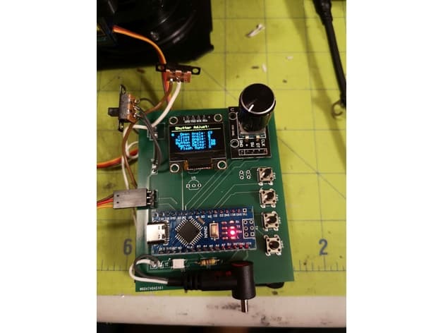 A control PCB on a cutting mat during bring-up, with an OLED display reading 'Shutter Adjust', a microcontroller dev board, power regulation, and four tactile buttons wired up for test.